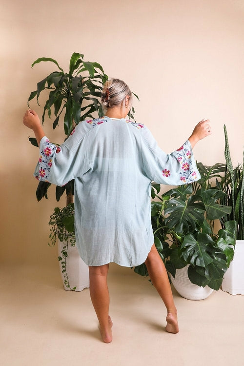 Woman wearing a light blue dress with floral sleeves in a room with plants
