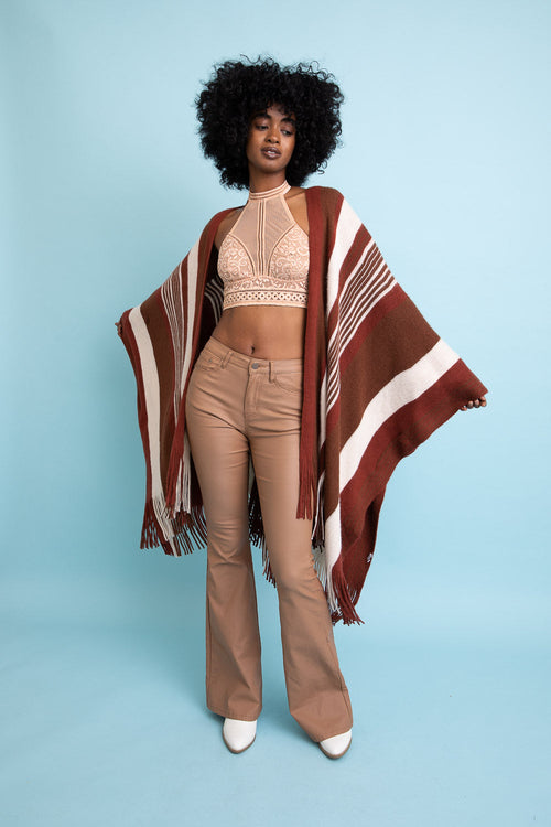 Woman wearing a patterned poncho over a beige outfit against a light blue background