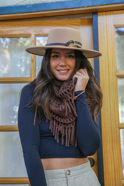 Woman wearing a beige hat and brown scarf standing in front of a wooden door.
