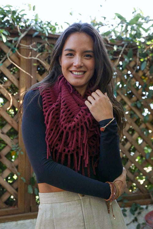 Woman wearing a dark blue top and beige pants with a red knitted scarf, standing outdoors.
