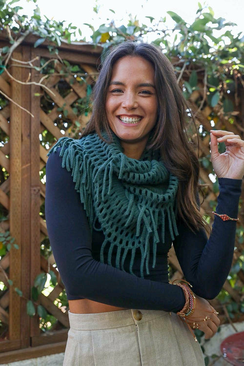 Woman wearing a green knitted scarf with a wooden lattice and foliage background
