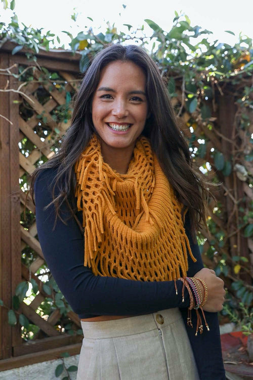 Woman wearing a mustard yellow scarf with a wooden lattice and greenery background