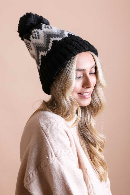 Woman wearing a black knit beanie with a pattern on a beige background