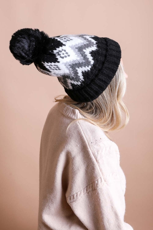 Person wearing a black knit beanie with a pom-pom on a beige background