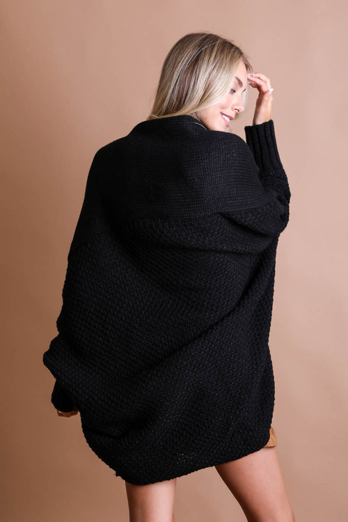 Woman wearing a black oversized sweater against a beige background