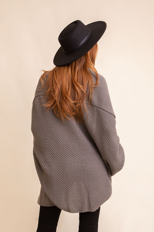 Person wearing a gray coat and black hat from behind on a beige background