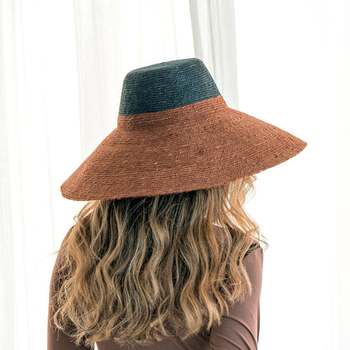 Person wearing a brown and green hat against a white curtain background