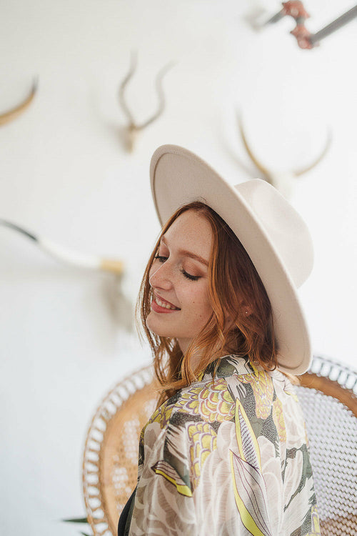 Woman wearing a white hat and patterned shirt in front of a decorative wall with antlers.