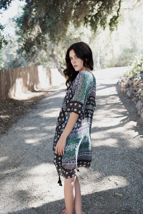 Woman in a patterned dress standing on a sunlit path with trees in the background