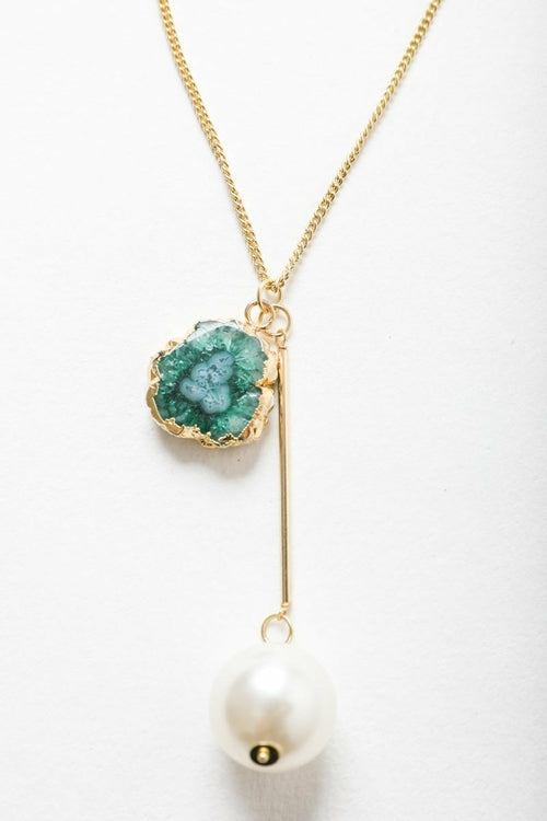 Gold necklace with green geode pendant and white pearl on a white background