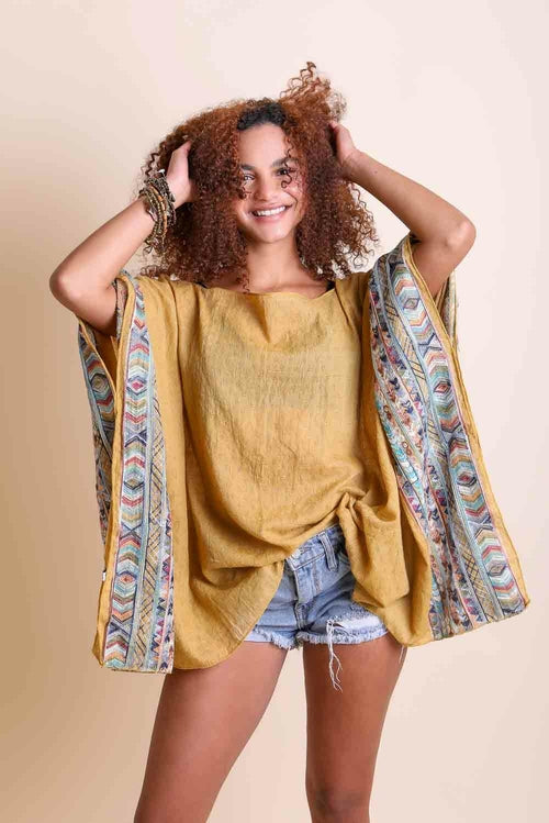 Woman wearing a mustard yellow top and patterned kimono over a beige background