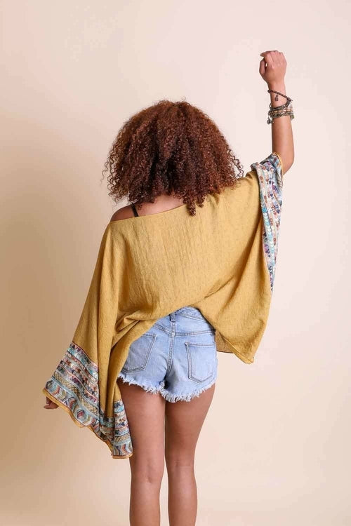 Person wearing a mustard yellow top with floral sleeves and denim shorts on a beige background