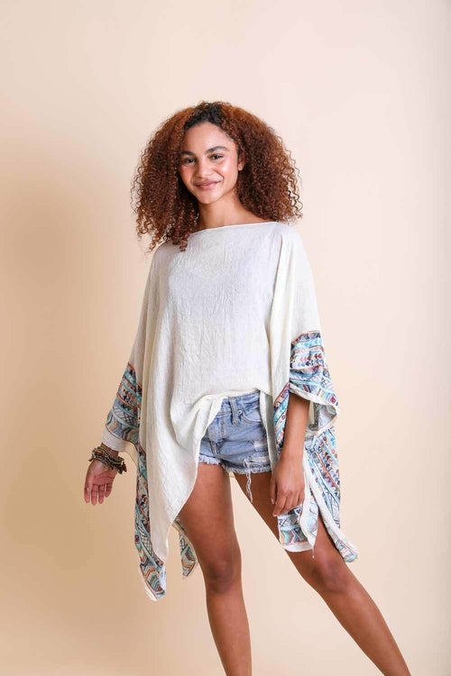 Woman wearing a white sweater with floral sleeves against a beige background