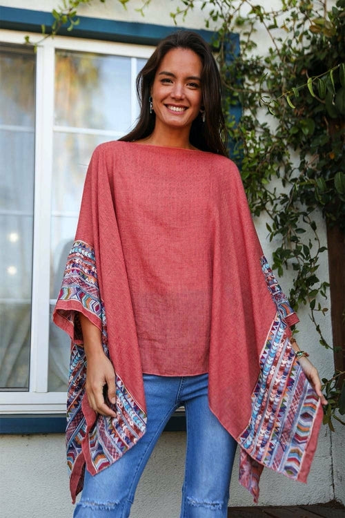 Woman wearing a pink poncho with colorful patterns standing outdoors.