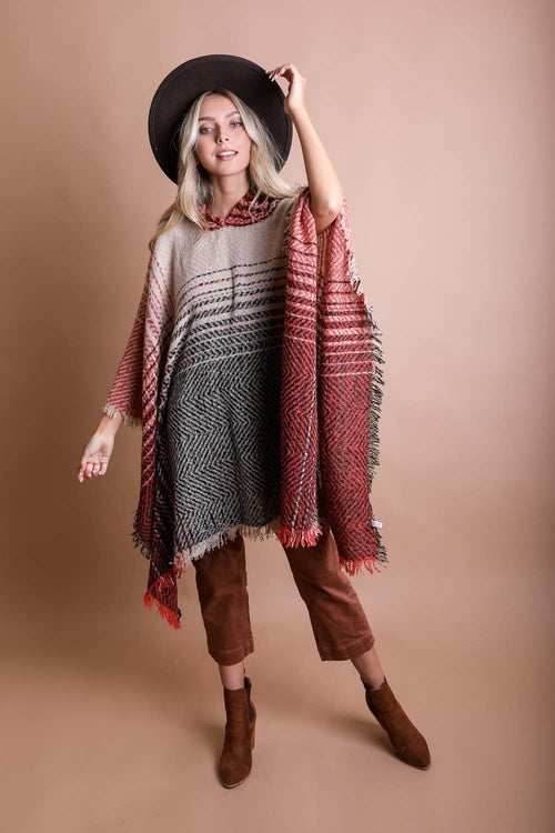 Woman wearing a patterned poncho, brown pants, and a black hat against a beige background