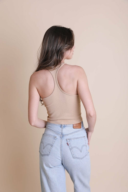 Woman wearing a beige tank top and light blue jeans against a beige background