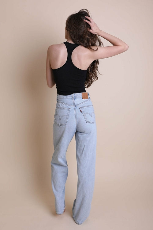 Person wearing light blue jeans and a black tank top against a beige background