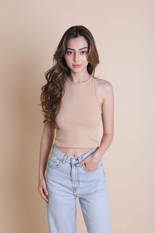 Woman wearing a beige sleeveless top and light blue jeans against a beige background