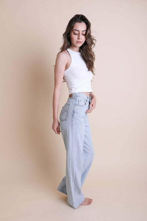 Woman wearing a white top and light blue jeans against a beige background