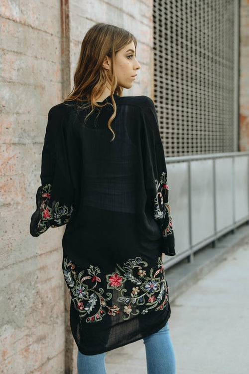 Woman wearing a black embroidered top against a textured wall.