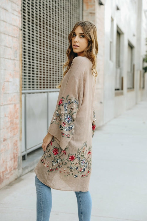Woman wearing a beige cardigan with floral embroidery walking down a street.