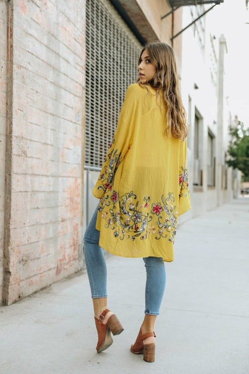 Woman wearing a yellow floral embroidered dress on a city street.