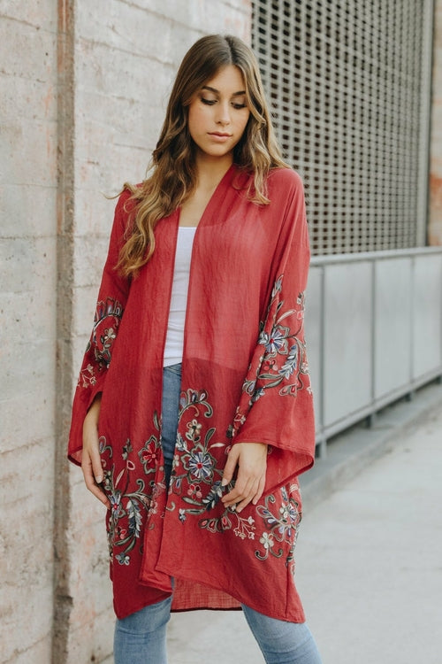 Woman wearing a red embroidered kimono against a neutral wall.