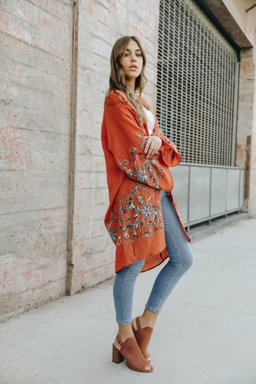 Woman wearing an orange embroidered kimono against a brick wall.