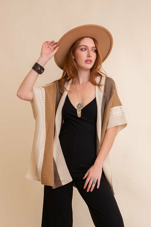 Woman wearing a beige cardigan and black outfit with a beige hat against a beige background