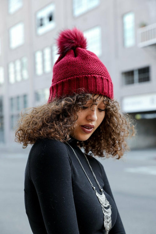 Person wearing a red knitted beanie with a pom-pom outdoors.