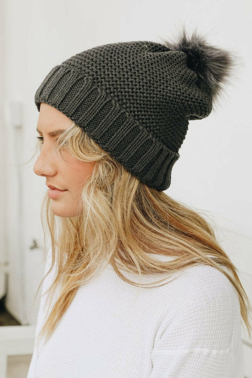 Woman wearing a dark gray knit beanie with a pom-pom on a white background
