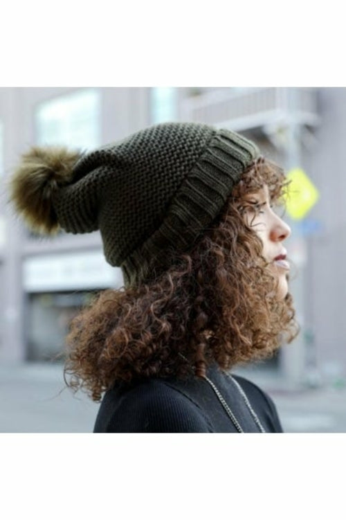 Person wearing a green knit beanie with a pom-pom in an urban setting
