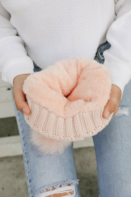 Person holding a pink knitted cup with a fluffy pink pom-pom.