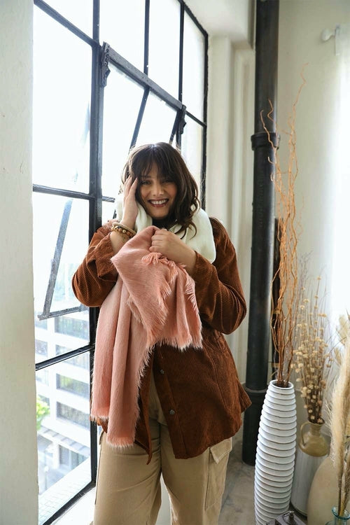 Woman holding a pink blanket indoors with large windows and decorative elements.