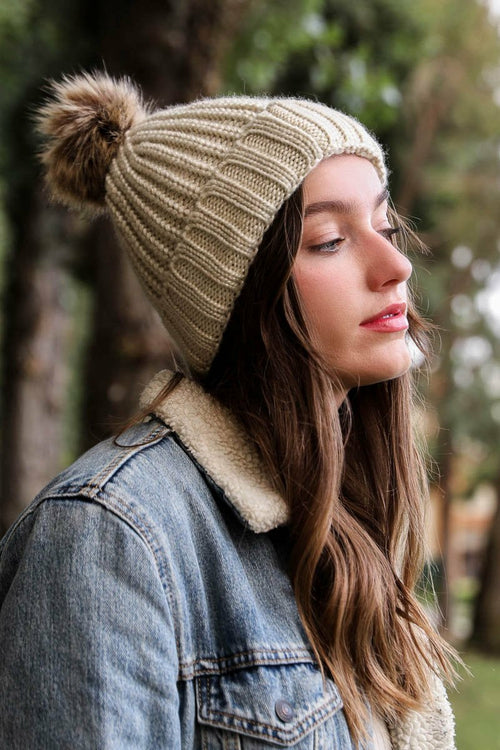 Woman wearing a beige knitted beanie with a pom-pom outdoors