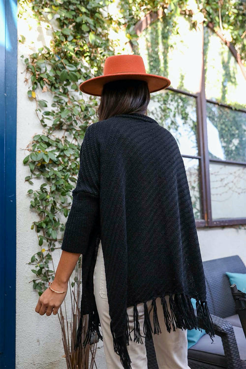 Person wearing a black poncho with fringe and an orange hat, standing outdoors.