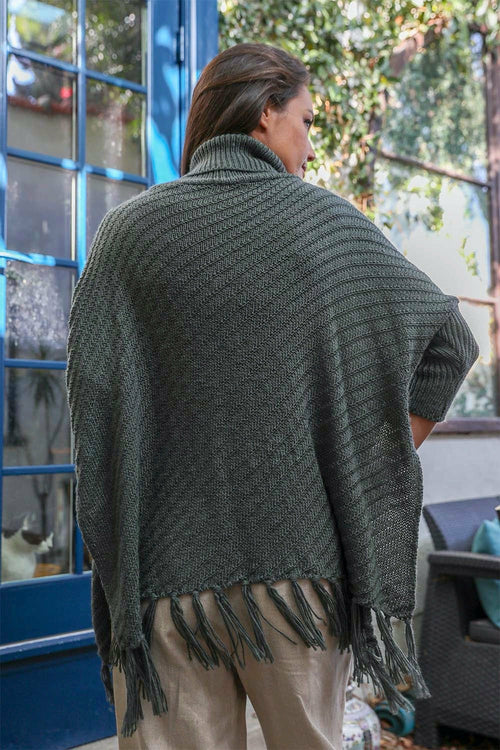 Person wearing a green poncho with fringe, standing outdoors.
