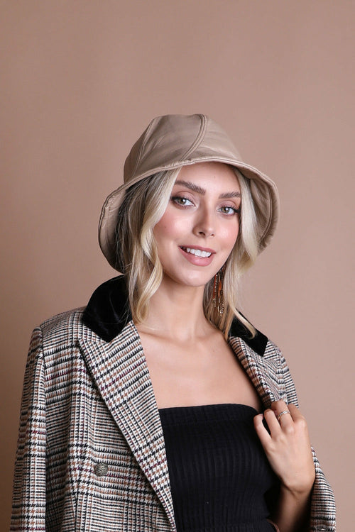Woman wearing a beige bucket hat and plaid coat against a beige background