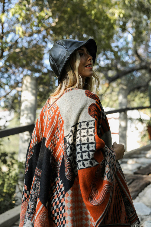 Person wearing a patterned poncho and bucket hat outdoors with trees in the background