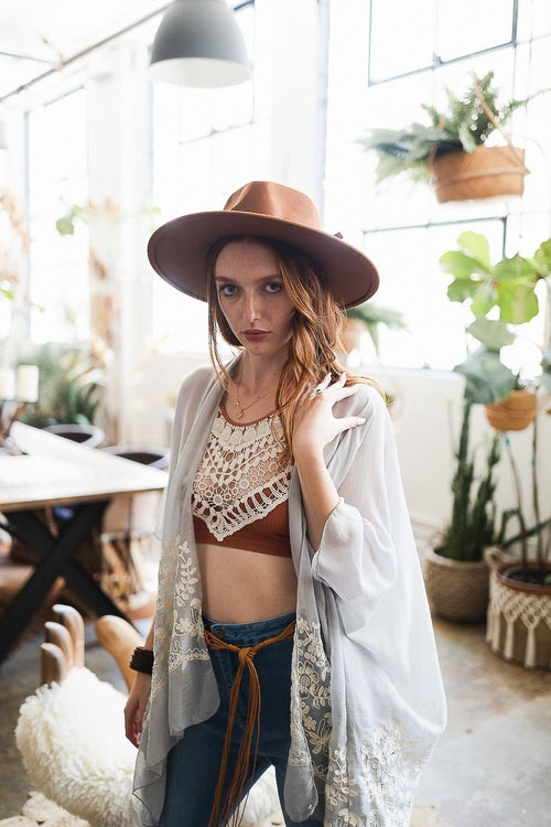Woman wearing a hat and casual outfit in a home setting with plants and furniture.