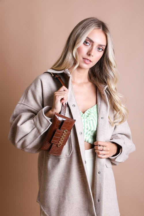 Woman holding a brown leather handbag against a beige background