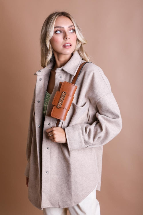 Woman wearing a beige coat holding a brown leather bag against a beige background