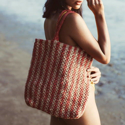 Woman holding a red and beige striped tote bag by the beach