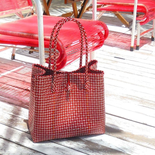 Red woven handbag on a wooden surface with red chairs in the background