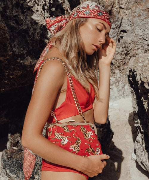 Woman in red bikini holding a patterned handbag against a rocky background