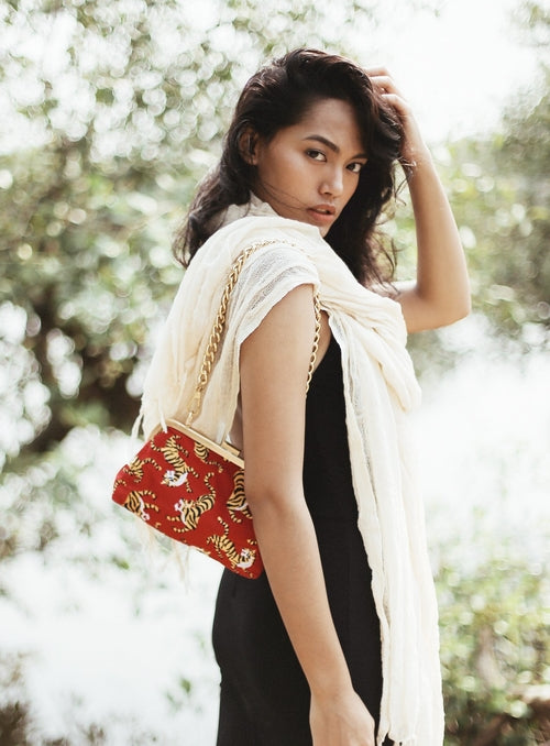 Woman holding a red handbag with gold accents outdoors