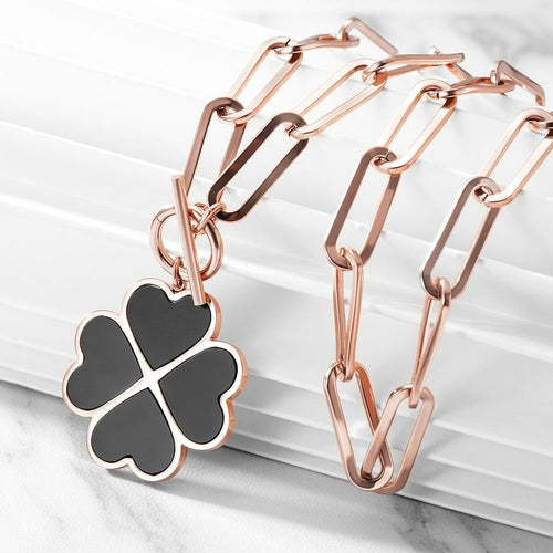 Rose gold bracelet with a black four-leaf clover charm on a marble surface