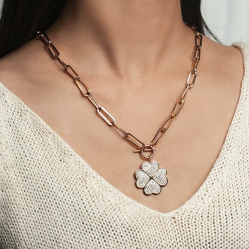 Rose gold chain necklace with a clover-shaped pendant worn by a person in a white sweater.