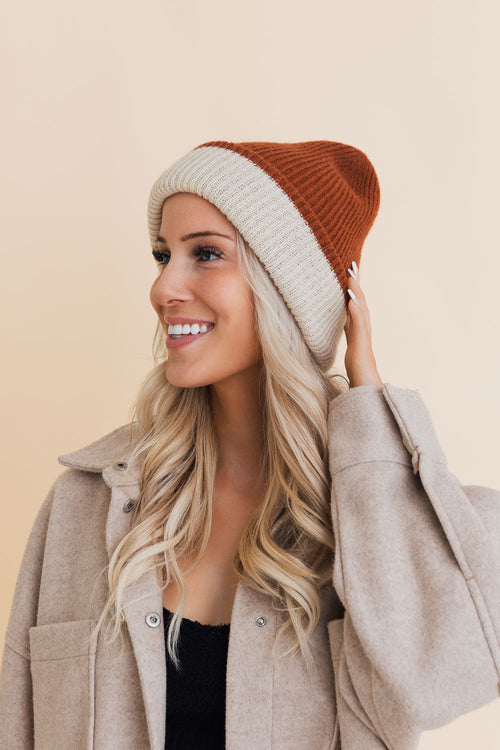 Woman wearing a two-tone beanie with beige and rust colors on a beige background