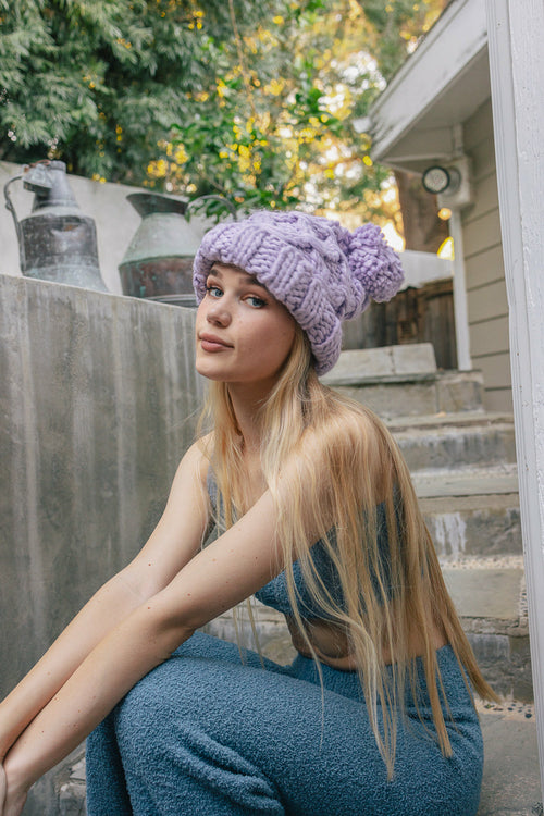 Woman wearing a purple knit beanie and blue dress sitting on steps outdoors.
